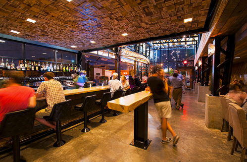 A lively bar interior with patrons at the counter, modern decor, and warm lighting creating a vibrant atmosphere.