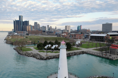 A lighthouse on the waterfront with a city skyline in the background, featuring parks and calm water.