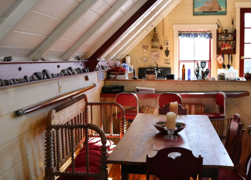 Cozy attic kitchen with wooden table, red chairs, and rustic decor, featuring natural light and a warm atmosphere.