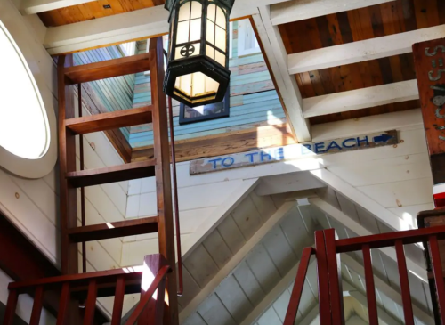 Interior view of a beach house with wooden beams, a lantern, and a sign pointing "To the Beach."