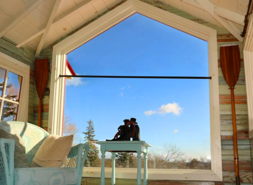 A cozy room with a large window showcasing a blue sky and trees, featuring a chair and a small table with a sculpture.