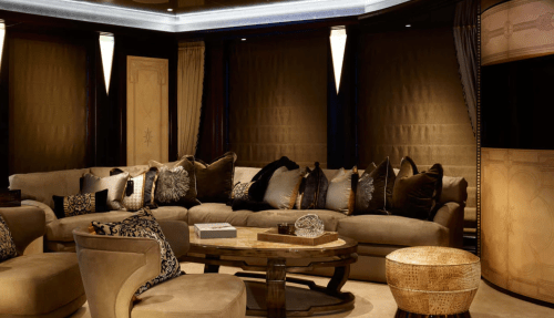Luxurious living room with a large sectional sofa, decorative pillows, and elegant lighting. Warm, rich color palette.