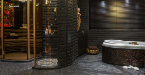 Luxurious bathroom featuring a modern shower, elegant tub, dark stone walls, and artistic decor.
