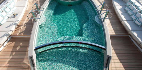 A luxurious boat deck featuring a turquoise pool surrounded by wooden flooring and lounge seating.