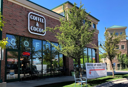 Exterior of a coffee shop named "Coffee & Cocoa," featuring large windows and a sign for drive-up service.