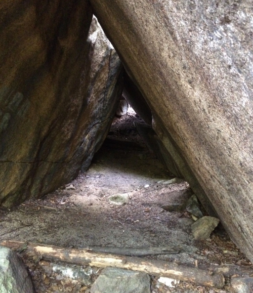 A narrow passage between large rocks, leading into a dimly lit space with dirt and scattered stones.