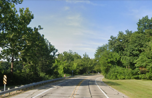 A winding road surrounded by lush green trees under a clear blue sky.