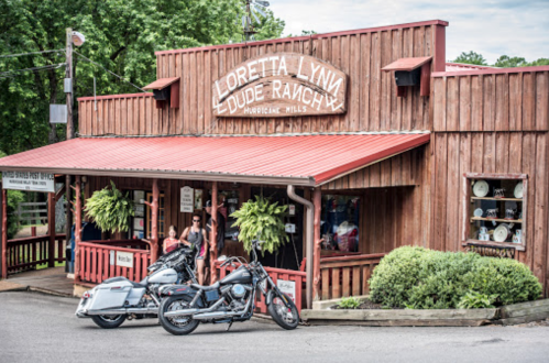 Exterior of Loretta Lynn's Dude Ranch with two motorcycles parked outside and visitors in front of the rustic wooden building.