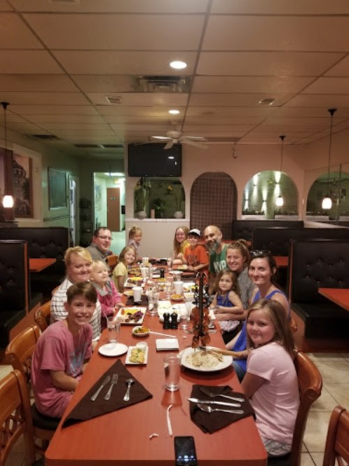 A large group of children and adults gathered around a table in a restaurant, enjoying a meal together.