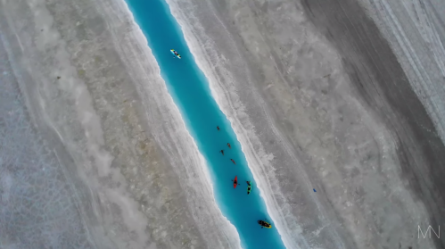 Aerial view of kayakers on a bright blue river surrounded by a light-colored, textured landscape.