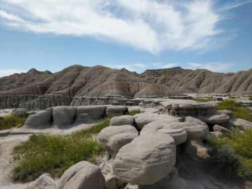 A rocky landscape with unique formations and sparse vegetation under a blue sky with wispy clouds.