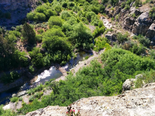Aerial view of a lush green valley with a winding stream surrounded by rocky terrain.