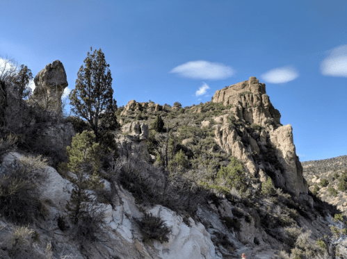 Rocky landscape with towering cliffs and scattered trees under a blue sky with a few clouds.