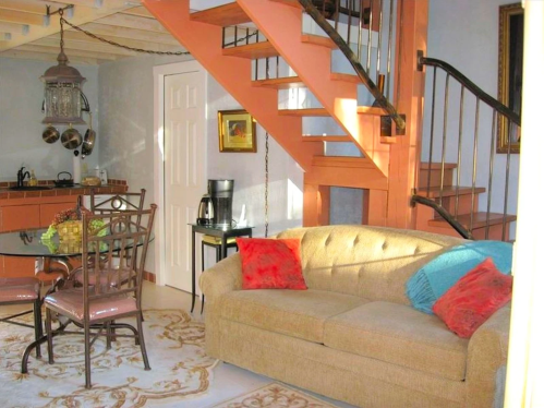 Cozy interior featuring a beige sofa, colorful cushions, a dining table, and a staircase in a well-lit space.