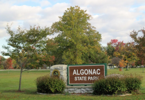 Sign for Algonac State Park surrounded by trees and greenery under a partly cloudy sky.