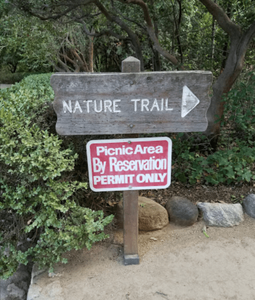 Wooden sign pointing to a nature trail, with a red sign below stating "Picnic Area By Reservation Permit Only."