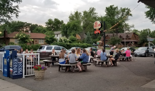A group of people enjoying ice cream at outdoor tables near a sign that reads "Ice Cream" in a cozy neighborhood setting.