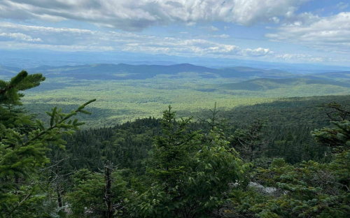 A panoramic view of lush green mountains and valleys under a partly cloudy sky.