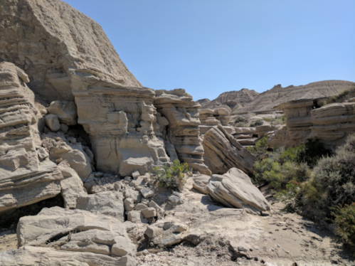 Rocky landscape with layered stone formations and sparse vegetation under a clear blue sky.