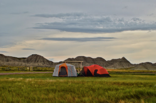 Two tents in a grassy area with rolling hills in the background under a cloudy sky.