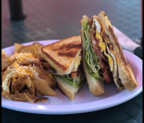 A plate with a grilled sandwich filled with lettuce, tomato, and bacon, alongside crispy potato wedges topped with cheese.