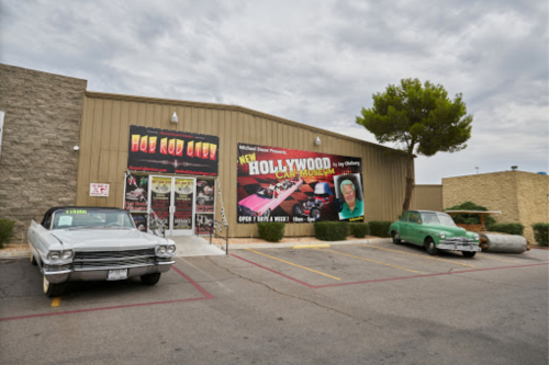 Exterior of a car museum featuring classic cars and a large banner promoting the Hollywood Car Museum.