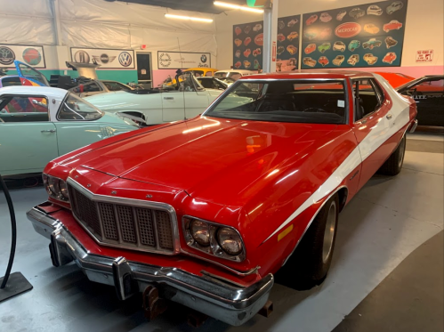 A red vintage Ford car displayed in a museum with other classic cars in the background.