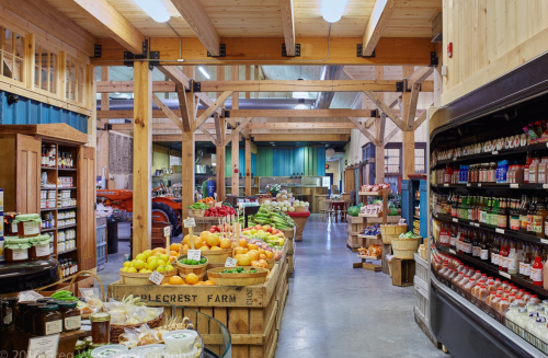 A spacious market interior with wooden beams, showcasing fresh produce, jars, and shelves of various goods.