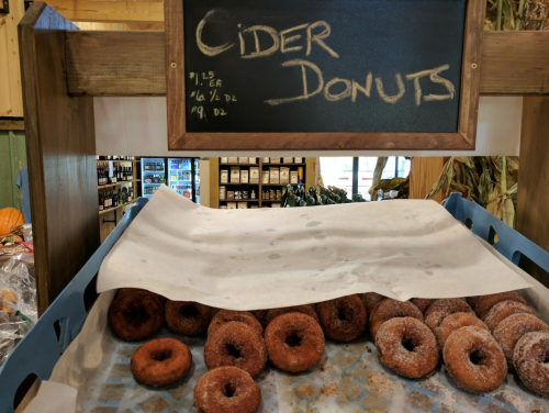 A display of cider donuts on a tray, with a chalkboard sign above listing prices.