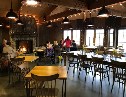 A cozy restaurant interior with wooden tables, a stone fireplace, and patrons enjoying their meals under warm lighting.