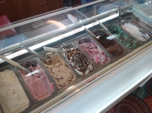 A display of various ice cream flavors in a glass case, with scoops and toppings visible.