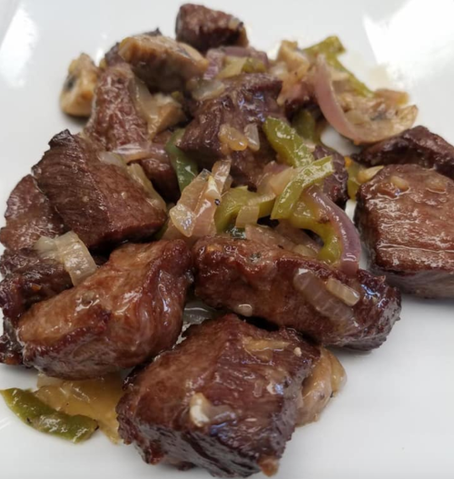 A plate of sautéed beef chunks with onions and green peppers, glistening with sauce.