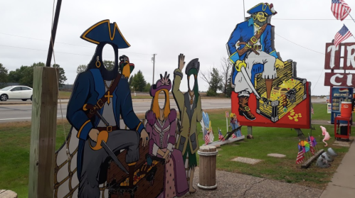 Colorful pirate-themed cutouts stand outside, featuring a pirate captain and a treasure chest, with a cloudy sky in the background.