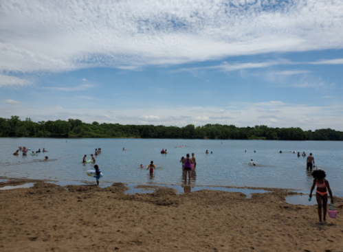 People enjoying a sunny day at a beach, playing in the water and relaxing on the sandy shore.