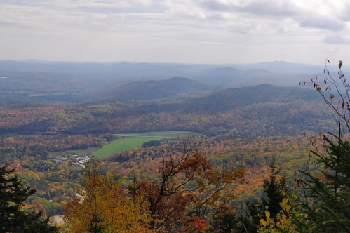 A panoramic view of rolling hills covered in vibrant autumn foliage under a cloudy sky.