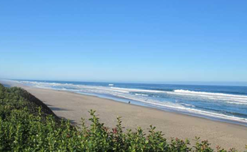 A serene beach scene with gentle waves, clear blue sky, and a person walking along the sandy shore.