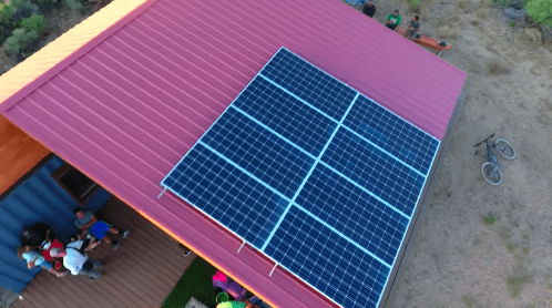 Aerial view of a house with a red roof and solar panels, surrounded by people and a bicycle nearby.