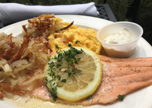A plate featuring salmon with lemon, hash browns, creamy mashed potatoes, and a side of dipping sauce.