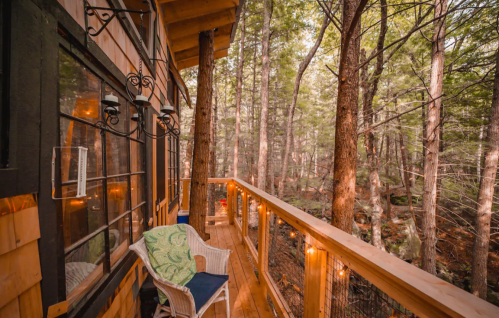 A cozy wooden balcony with a chair, surrounded by tall trees and soft lighting in a serene forest setting.