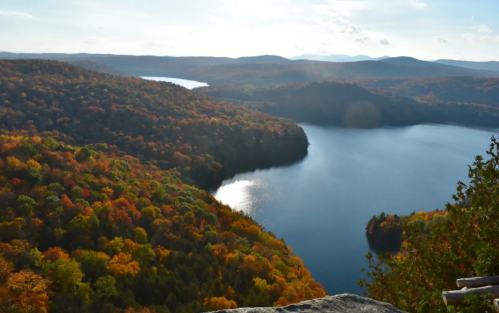 A scenic view of a lake surrounded by vibrant autumn foliage and rolling hills under a bright sky.