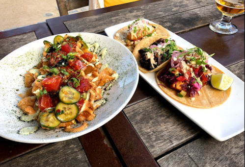 A plate of nachos topped with vegetables and sauce, alongside two tacos with various fillings and garnishes.