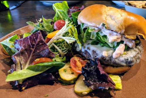 A juicy burger with melted cheese, lettuce, and sauce, served with a side of mixed greens and cherry tomatoes.