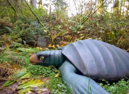 A large, realistic turtle sculpture in a lush, green forest setting with a sign nearby.