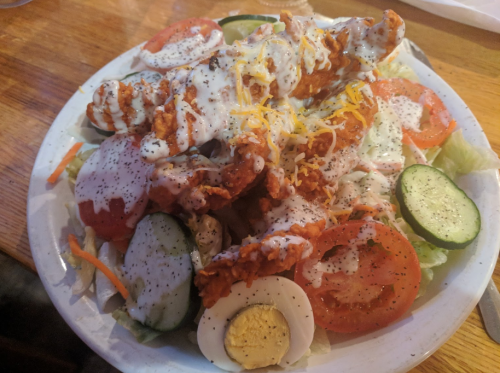 A colorful salad topped with crispy chicken, cheese, tomatoes, cucumbers, and drizzled with creamy dressing.