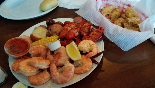 A seafood platter with shrimp, crawfish, potatoes, corn, and dipping sauce, alongside a basket of fried food.