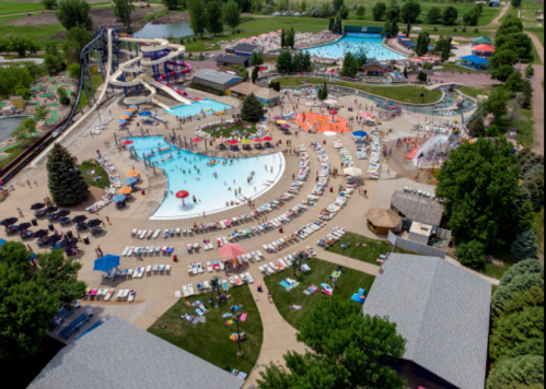 Aerial view of a water park with pools, slides, and sun loungers, surrounded by trees and green spaces.