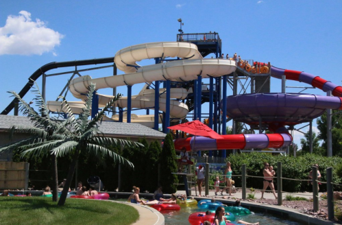 A water park featuring colorful slides, a lazy river, and people enjoying the sunny day.