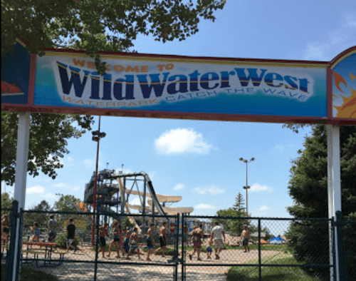 Entrance sign for Wild Water West waterpark, with visitors enjoying the attractions on a sunny day.