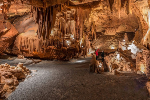 A dimly lit cave with stalactites and stalagmites, featuring a person exploring the rocky terrain.