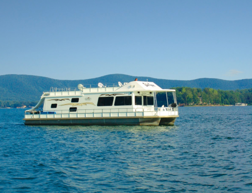 A houseboat floats on calm water with mountains in the background under a clear blue sky.